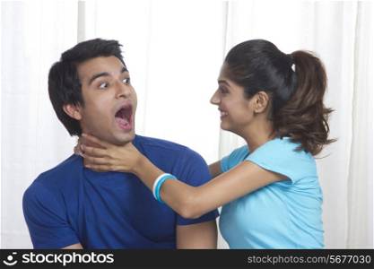 Playful young woman gripping man&rsquo;s neck at home