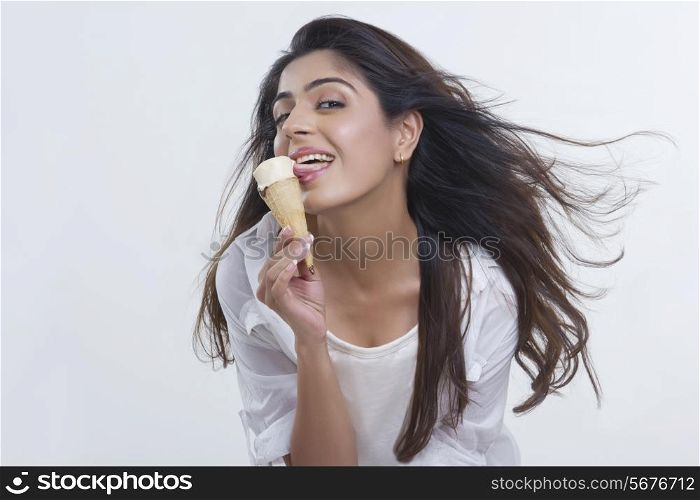 Playful young woman licking ice-cream cone over white background