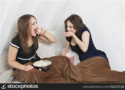 Playful young women eating popcorn in bed