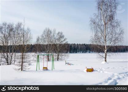 Playground with swings, covered with snow on a Sunny winter day.