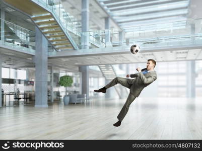 Playing ball in office. Emotional businessman playing soccer ball in modern office