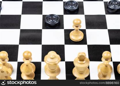 playing by different rules on the same board - black checkers and white chess figures on black white chessboard, above view of pawn and checkers piece moves closeup (focus on the pawn)