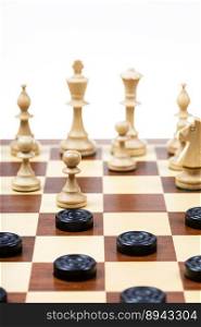 playing by different rules on the same board - black checkers and white chess figures on wooden chessboard, gameboard with chess and checkers playing closeup  focus on front checkers disc 