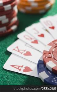Playing cards making royal flush in hearts by poker chips (close up/selective focus)