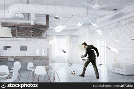 Playing football in office. Businessman in suit in modern office jumping to hit soccer ball