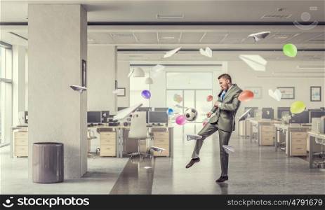 Playing football in office. Businessman in suit in modern office jumping to hit soccer ball