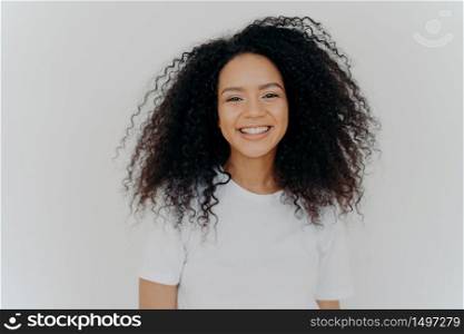 Pleasant looking young woman has toothy smile, happy face expression, laughs at something funny, shows white perfect teeth, dressed casually, isolated over white background, glad to start new life