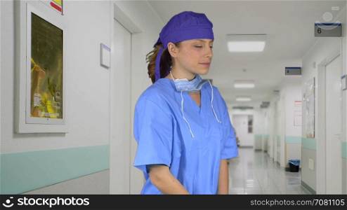 Pleased female medical professional w/ hand on chin in the hall