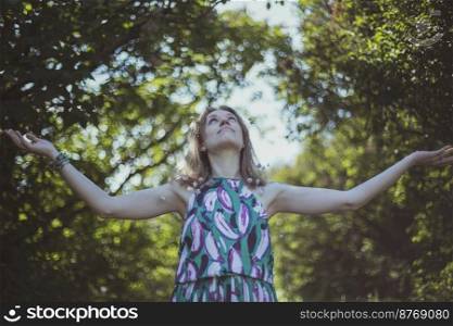 Pleased girl in summer dress spreading arms scenic photography. Picture with garden landscape on background. High quality wallpaper. Photo concept for ads, travel blog, magazine, article. Pleased girl in summer dress spreading arms scenic photography