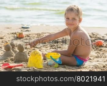 Pleased with the child on a sandy beach at the water points at cakes hired by sand