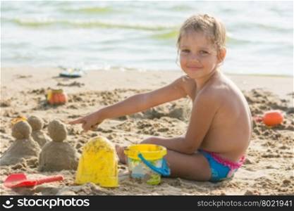 Pleased with the child on a sandy beach at the water points at cakes hired by sand
