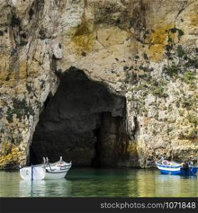 Pleasure boats at the rugged coastline delineated by sheer limestone cliffs, and dotted with deep caves on Malta. The Inland Sea is a lagoon of seawater on the island of Gozo linked to the Mediterranean Sea through an opening formed by a narrow natural arch.