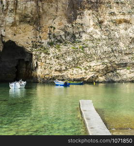 Pleasure boats at the rugged coastline delineated by sheer limestone cliffs, and dotted with deep caves on Malta. The Inland Sea is a lagoon of seawater on the island of Gozo linked to the Mediterranean Sea through an opening formed by a narrow natural arch.