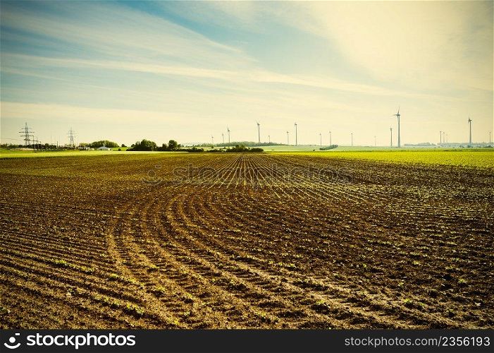 Plowed fields in Austrian landscape with modern wind turbines producing energy. Vintage style 