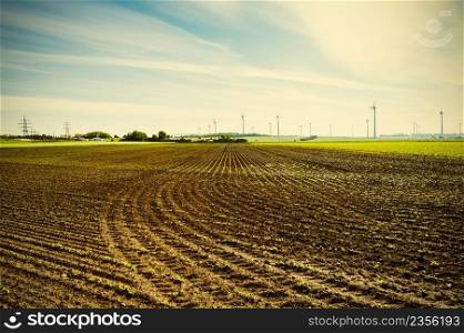 Plowed fields in Austrian landscape with modern wind turbines producing energy. Vintage style 