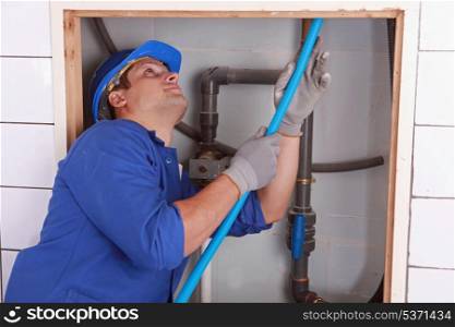 Plumber feeding blue flexible pipe behind a tiled wall