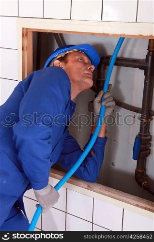 Plumber feeding blue pipe behind a tiled wall