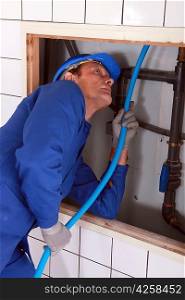 Plumber feeding blue pipe behind a tiled wall