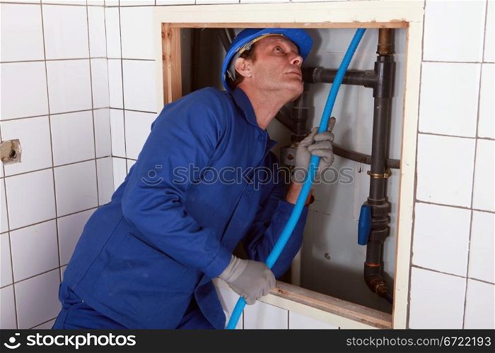 Plumber feeding blue pipe behind a wall