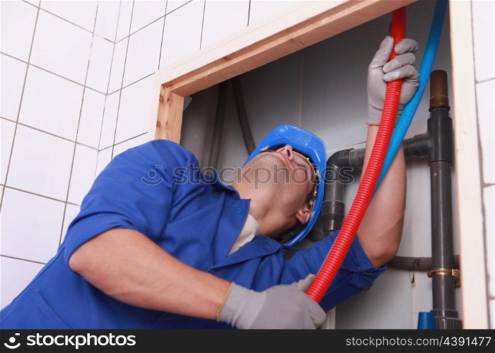Plumber feeding flexible pipes behind a tiled wall