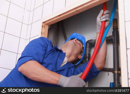 Plumber feeding flexible pipes behind a tiled wall