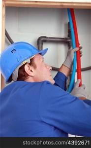 Plumber feeding hot and cold pipes behind a wall