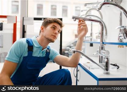 Plumber in uniform at showcase in plumbering store. Man with notebook buying sanitary engineering in shop, water taps and faucets choice. Plumber in uniform at showcase in plumbering store