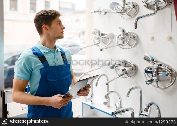 Plumber in uniform at showcase in plumbering store. Man with notebook buying sanitary engineering in shop, water taps and faucets choice