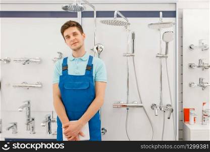 Plumber in uniform at showcase with boilers in plumbering store. Man with notebook buying sanitary engineering in shop, water taps and faucets choice. Plumber at showcase with boilers, plumbering store