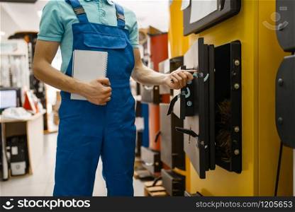 Plumber in uniform buying boiler with furnace at showcase in plumbering store. Man with notebook buying sanitary engineering in shop, water heater choice. Plumber buying boiler with furnace, plumbering