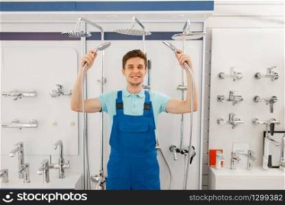 Plumber in uniform choosing shower at showcase in plumbering store. Man buying sanitary engineering in shop, bathroom equipment choice