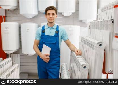 Plumber in uniform choosing water heating radiator at showcase in plumbering store. Man buying sanitary engineering in shop. Plumber in uniform choosing water heating radiator