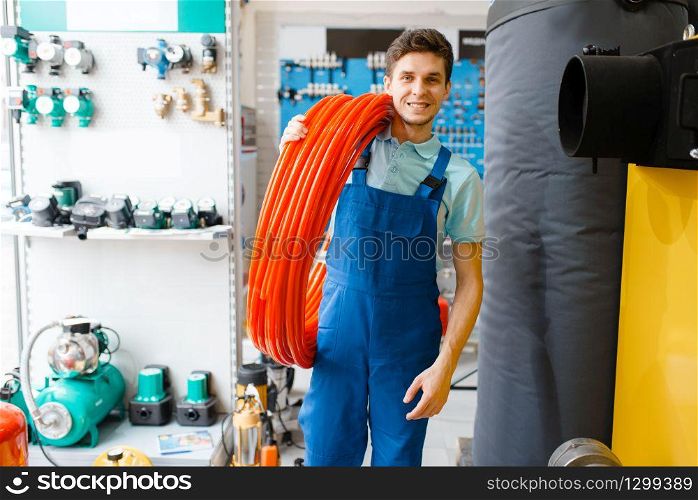 Plumber in uniform holds pipe roll in plumbering store. Man buying sanitary engineering in shop