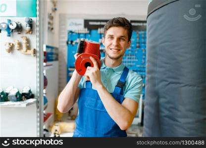 Plumber in uniform holds water pump at showcase in plumbering store. Man buying sanitary engineering in shop. Plumber holds water pump, plumbering store