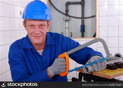 Plumber sawing length of plastic pipe