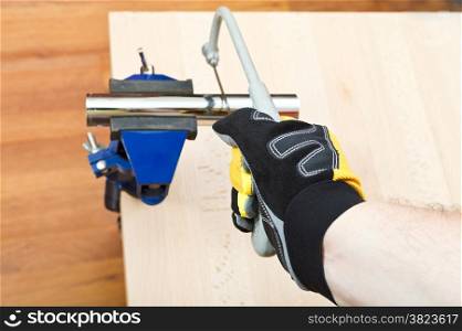 plumber sawing plumbing drain pipe gripped in vice on wooden table by hacksaw