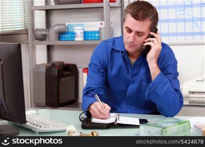 Plumber taking a call in an office and making an appointment in his diary