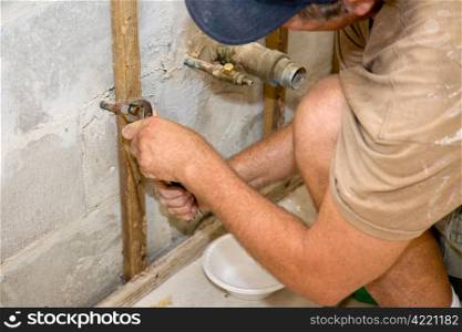 Plumber using channel-lock pliers to attach a nut to a water pipe. He has a bowl beneath to catch any remaining water. Authentic and accurate content depiction.