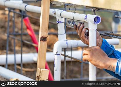 Plumber Using Level While Installing PVC Pipe At Construction Site.