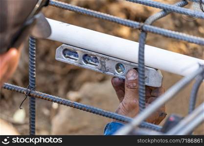 Plumber Using Level While Installing PVC Pipe At Construction Site.