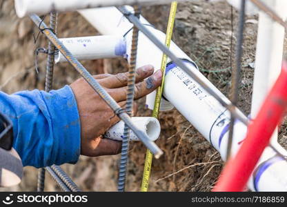 Plumber Using Tape Measure While Installing PVC Pipe At Construction Site.