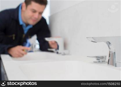 Plumber Working On Sink Using Wrench In Bathroom