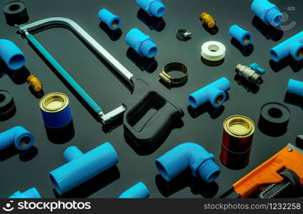 Plumbing tools. Plumber equipment. Blue PVC pipe fittings, hacksaw, glue can, and pipe wrench. House plumbing repair and maintenance service. DIY tools for plumbing work isolated on dark background.