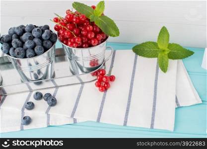 Plums, red currants and blueberries in small metal bucket on the wooden table.