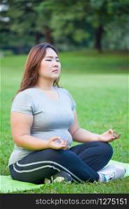 Plus size asian woman practicing yoga on green grass in the park
