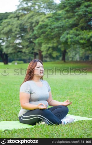 Plus size asian woman practicing yoga on green grass in the park