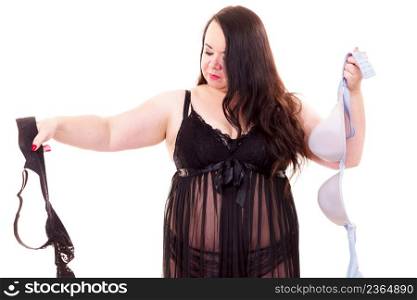 Plus size fat woman wearing lingerie holding black and bright bras, choosing witch bra to wear, on white. Bosom, brafitting, underwear and female dilemmas.. Woman choosing witch bra to wear.