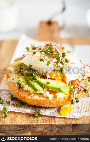 Poached egg with avocado, ricotta cheese and radish sprouts on burger bun. Healthy sandwich with bread, fresh avocado, poached egg and cheese garnished with radish microgreens. Healthy eating concept.