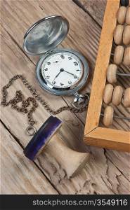 pocket watch, abacus and stamp on a wooden table