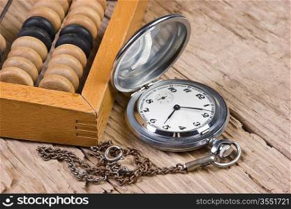 pocket watch and abacus on a wooden table